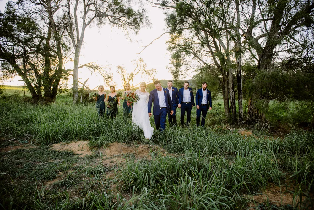 A group of wedding party members walking through a forested area at Lilydale Estate, 9Dorf Farms.